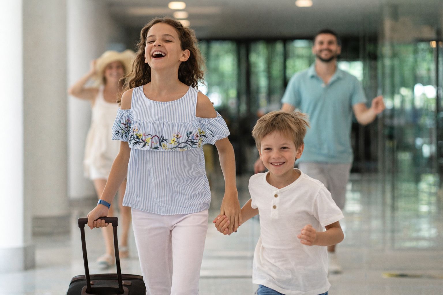 Deux enfants joyeux courent dans le hall d'un hôtel avec une valise.
