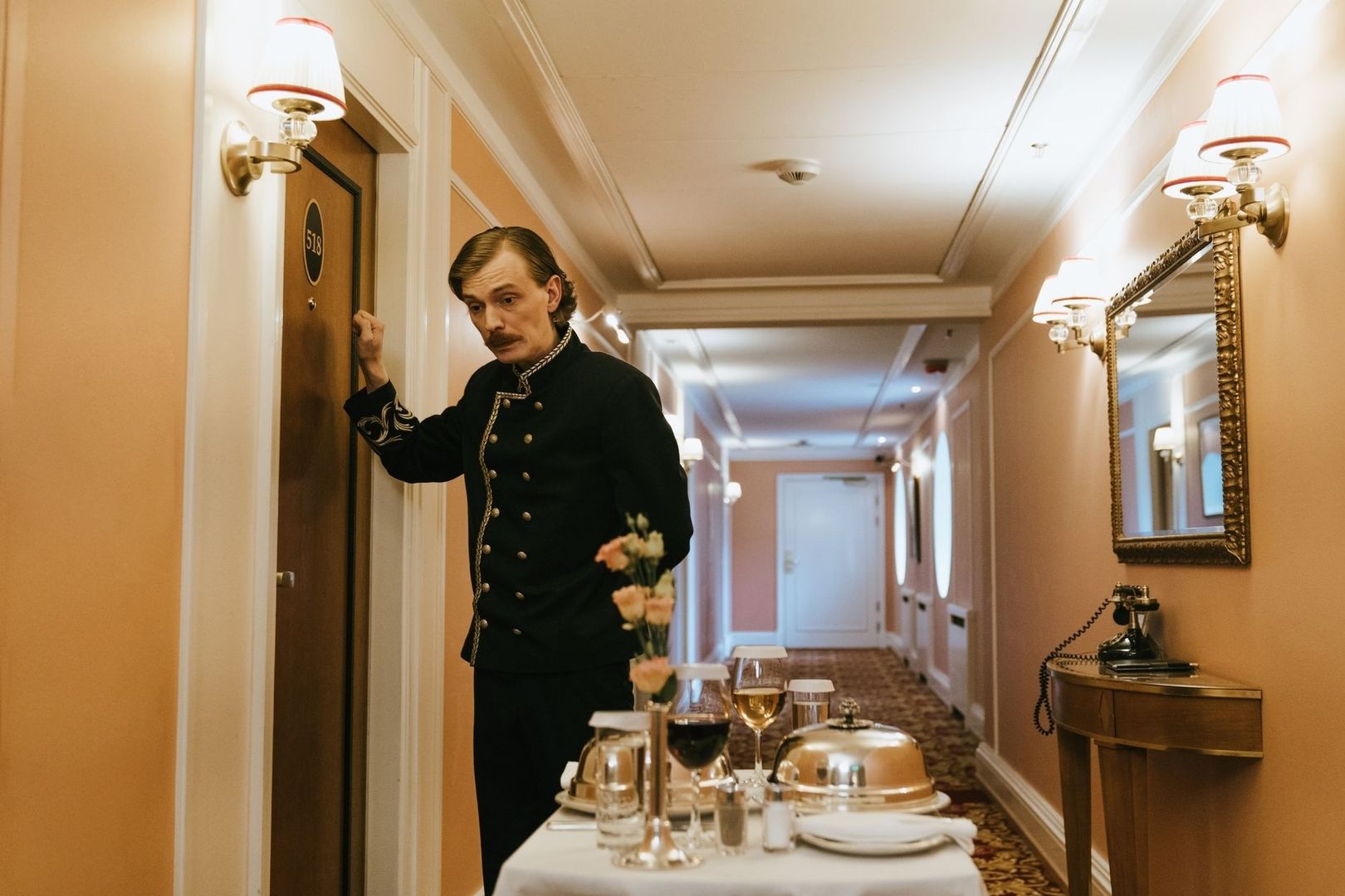 Concierge en uniforme devant une chambre, avec un chariot de service